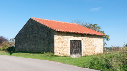 Fototapeta na wymiar Establo rústico de piedra con puerta y tejado junto a carretera
