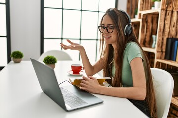 Young hispanic woman having video call sitting on table at home