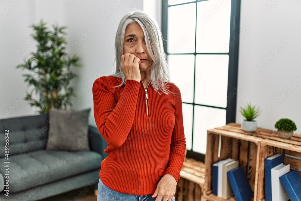 Wall mural Middle age grey-haired woman wearing casual clothes standing at home looking stressed and nervous with hands on mouth biting nails. anxiety problem.