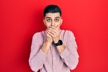 Handsome man with beard wearing casual red shirt shocked covering mouth with hands for mistake. secret concept.