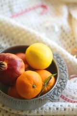 Silver bowl with various fruit, soft blanket and various Christmas decorations. Hygge at home. Selective focus.