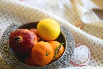 Silver bowl with various fruit, soft blanket and various Christmas decorations. Hygge at home. Selective focus.