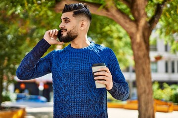 Young arab man talking on the smartphone drinking coffee at park