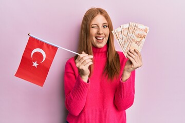 Young irish woman holding turkey flag and liras banknotes winking looking at the camera with sexy expression, cheerful and happy face.