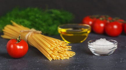 spaghetti pasta, red tomatoes, garlic and herbs on a table on a dark background