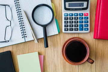 Cup of coffee, notebook with pen, calculator, glasses and other accessories on the desktop