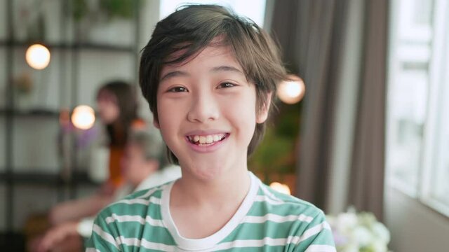 portrait of young child asian boy looking at camera smiling cheerful in living room at home,pov shot of asian son fun playful in christmas weekend vacation with family in apartment at home