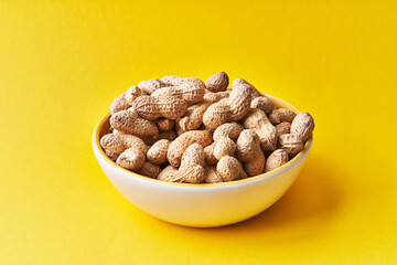  Bowl of peanuts with shell on a yellow background