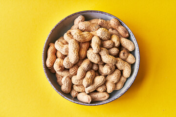 Bowl of peanuts with shell on a yellow background
