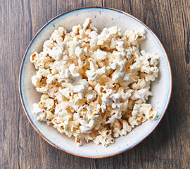  Bowl of salty popcorns on a wooden surface