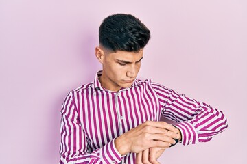 Young hispanic man wearing casual clothes checking the time on wrist watch, relaxed and confident