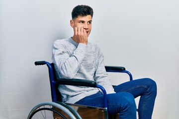 Young hispanic man sitting on wheelchair looking stressed and nervous with hands on mouth biting nails. anxiety problem.