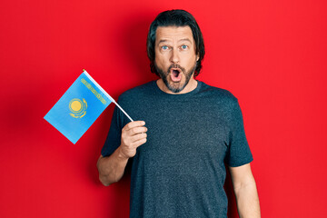 Middle age caucasian man holding kazakhstan flag scared and amazed with open mouth for surprise, disbelief face