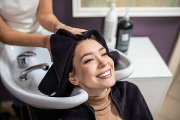 Fototapeta na wymiar Professional hairdresser washing hair of a beautiful young adult woman in hair salon.