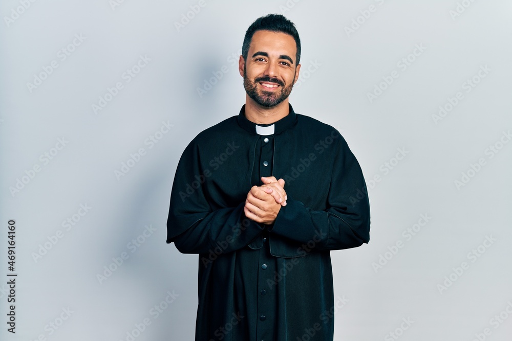 Canvas Prints Handsome hispanic man with beard wearing catholic priest robe with hands together and crossed fingers smiling relaxed and cheerful. success and optimistic