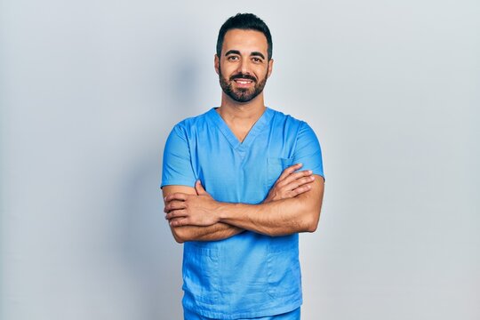 Handsome hispanic man with beard wearing blue male nurse uniform happy face smiling with crossed arms looking at the camera. positive person.