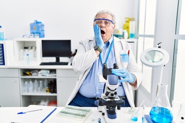 Senior caucasian man working at scientist laboratory afraid and shocked, surprise and amazed expression with hands on face