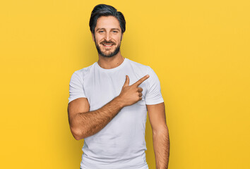 Young hispanic man wearing casual white t shirt cheerful with a smile of face pointing with hand and finger up to the side with happy and natural expression on face