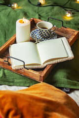 Fototapeta na wymiar Cup of coffee and notebook with candle in tray in bed