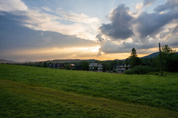 Fototapeta premium Green meadow field showing countryside view against dramatic sunrise or sunset, in Zakopane, Poland, Europe