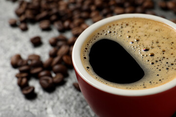 Cup of aromatic coffee and beans on grey table, closeup. Space for text
