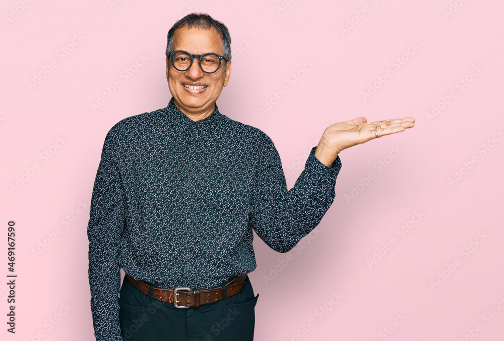 Canvas Prints Middle age indian man wearing casual clothes and glasses smiling cheerful presenting and pointing with palm of hand looking at the camera.