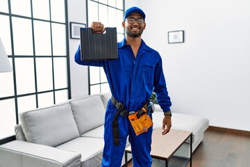 Young indian technician holding toolbox and screwdriver at house looking positive and happy standing and smiling with a confident smile showing teeth