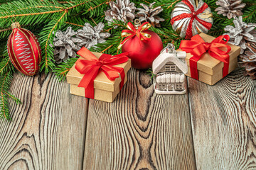 festive christmas and new year background with copy space, fir branches, christmas decorations, pine cones, toy house and gifts on a vintage wooden table