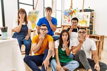 Group of people sitting at art studio covering mouth with hand, shocked and afraid for mistake. surprised expression