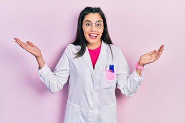 Young hispanic girl wearing scientist uniform celebrating victory with happy smile and winner expression with raised hands