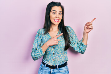 Young hispanic girl wearing casual clothes smiling and looking at the camera pointing with two hands and fingers to the side.