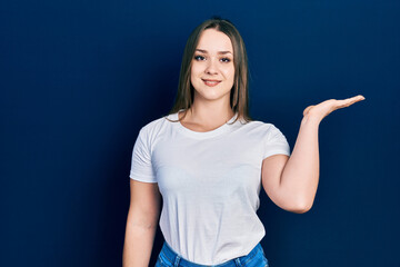 Fototapeta premium Young hispanic girl wearing casual white t shirt smiling cheerful presenting and pointing with palm of hand looking at the camera.
