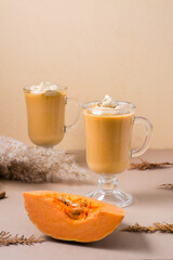 Pumpkin whipped coffee with cinnamon in glasses and a slice of pumpkin on a beige background. Autumn hot homemade drinks. Vertical view