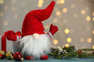Cute Christmas gnome, gift box and festive decor on turquoise wooden table against blurred lights