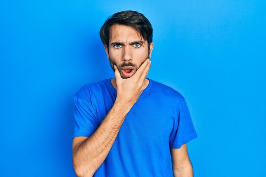 Young hispanic man wearing casual clothes looking fascinated with disbelief, surprise and amazed expression with hands on chin