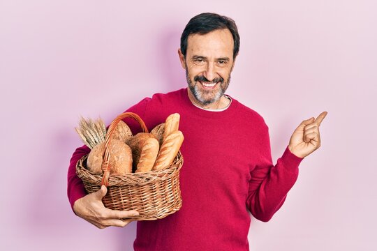 Middle age hispanic man holding wicker basket with bread smiling happy pointing with hand and finger to the side