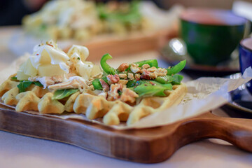 close up details of healthy tasty belgian waffle with green vegetables, nuts and cheese on wooden board