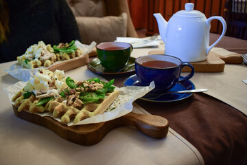 healthy tasty belgian waffle with green vegetables, nuts and cheese on wooden board hot coffee in cups and white teapot