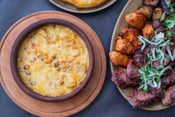 baked suluguni cheese with tomatoes of national Georgian cuisine in earthenware on ketsi with chicken and pork kebabs