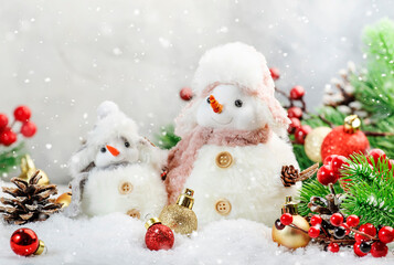 Christmas snow composition with two cute snowmen in hats and scarves in snowdrift and fir branches on gray background