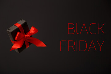 Black Friday. Beautiful flying black gift box with red bow floating in air on black background. Black friday sale, discount, shopping concept.