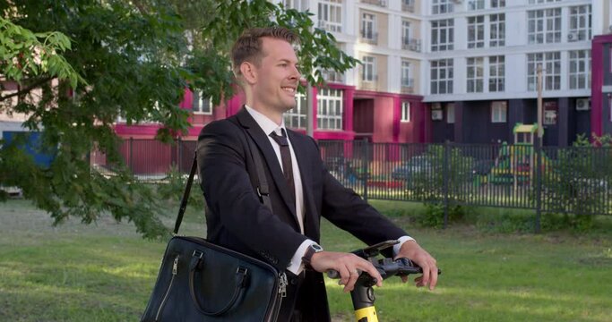 Modern caucasian male checking the time and preparing to drive an electric scooter, going for work, dressed in formal suit, suit, in city street at summer day. people, eco-friendly lifestyle