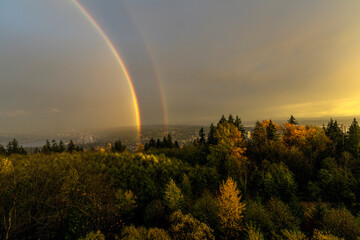 Double rainbow over Fraser Valley against dark rainclouds on a misty day as seen from Burnaby Mountain, BC.