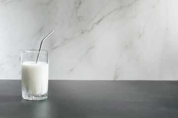 Glass of milk with a straw, reusable on a white and gray background. Place for your text. Copy...
