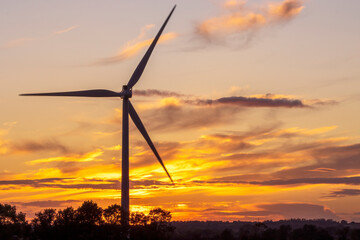 Fototapeta na wymiar A wind turbine generating sustainable energy silhouetted against a colourful sunset sky