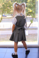 Back view of upset little girl blond in grey dress look in window thinking of future happy life, small child wait