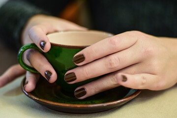 young female hands with dark nail polish holding beautiful dark green coffee cup on platter with hot green tea