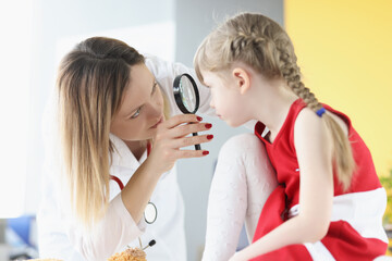 Ophthalmologist conducts medical examination of girl eye through magnifying glass