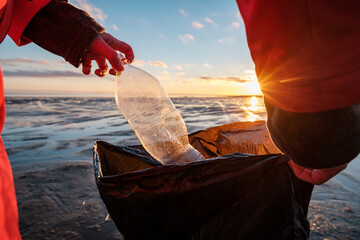 A woman cleans the bank of plastic bottles and puts the trash in a garbage bag. Environmental...