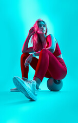 Female taking a break from cross workout sit on fitness medicine ball. Neon blue light modern concept